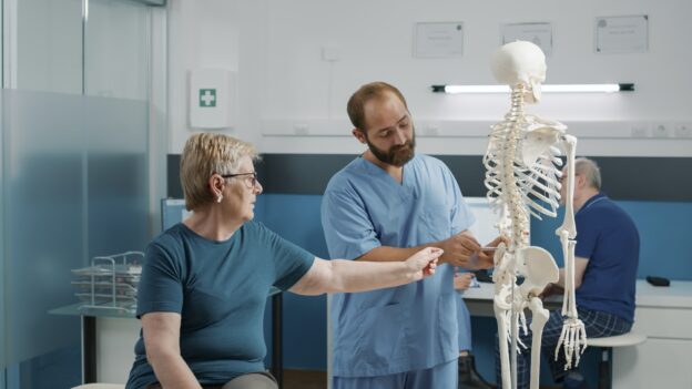 Osteopath explaining orthopedic diagnosis on human skeleton